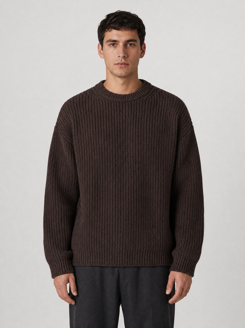 Man wearing a brown drop shoulder chunky knit sweater, front view on a light grey studio background
