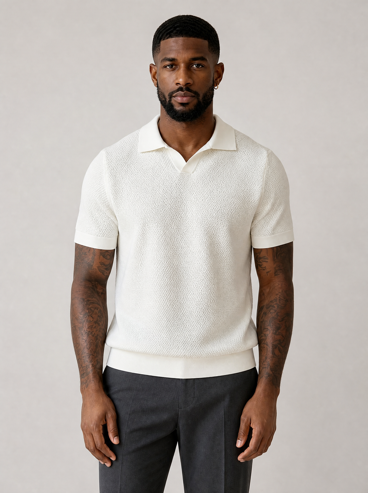 Man wearing a cream textured knit short sleeve polo, front view on a light grey studio background