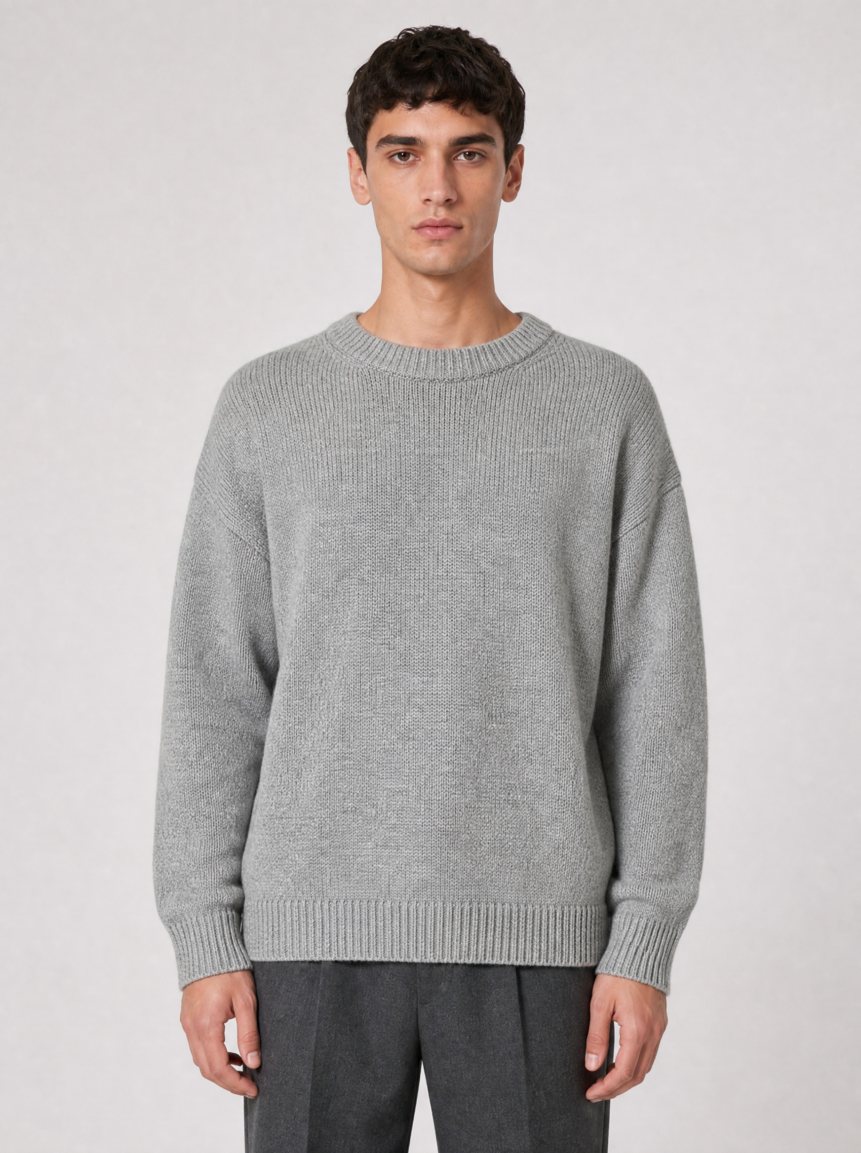 Man wearing a light grey oversized knit sweater, front view on a light grey studio background